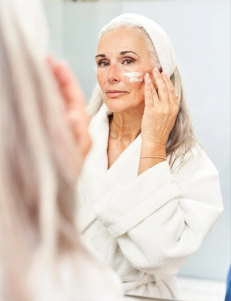 mujer mayor mirandose al espejo aplicandose productos de skincare
